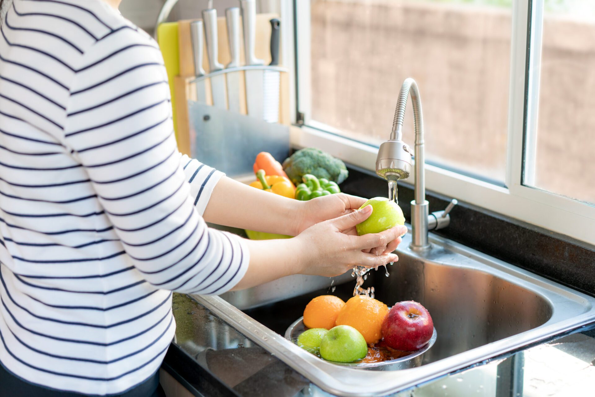close up hands washing apples and other fruit in kitchen sink. professional plumbing services built for long-term performance