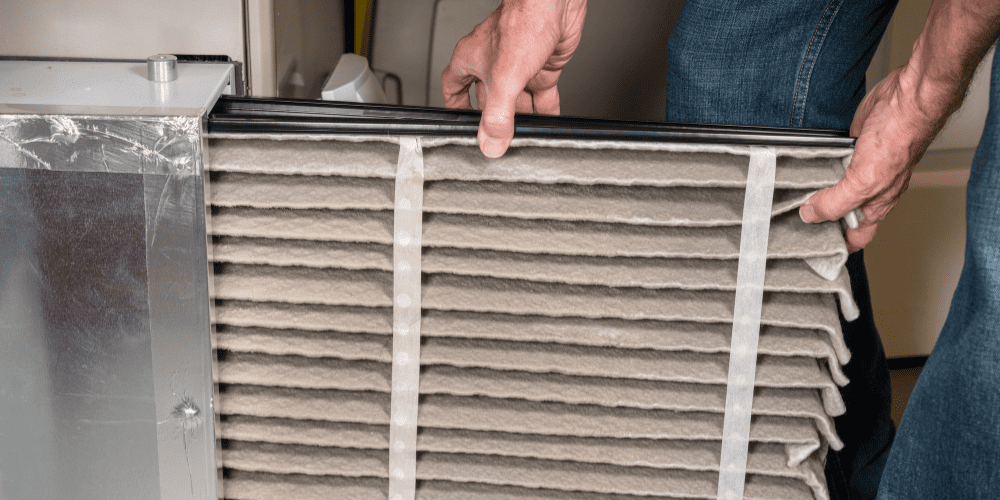 An HVAC technician removing a dirty air filter to replace with a clean new filter for better indoor air quality - Three Benefits of Replacing Your Air Filters Regularly - Allen Heating Cooling and Plumbing